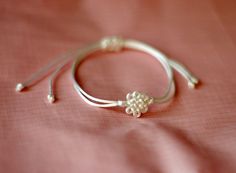 a close up of a white bracelet on a pink cloth with a flower charm in the middle