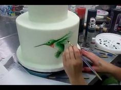 a woman is painting a hummingbird on a white cake