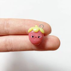 a hand holding a tiny pink apple with a yellow horn on it's head