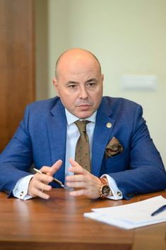 a man in a blue suit sitting at a table with his hands out to the side