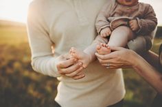 a woman holding a baby in her arms while standing next to a man's hand