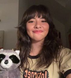 a woman holding a stuffed raccoon in her hand and smiling at the camera