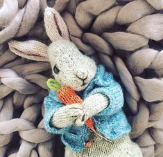 a knitted bunny holding a carrot in it's lap, surrounded by yarn