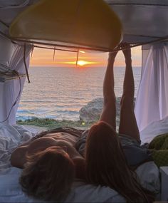 a woman laying on top of a bed under a canopy next to the ocean at sunset