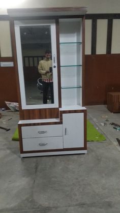 a man is standing in front of a cabinet with drawers and a mirror on it