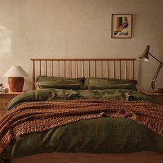 a bed with green sheets and pillows in a bedroom next to a lamp on a table