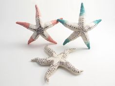 three starfishs are sitting side by side on a white surface, one is pink and the other is blue