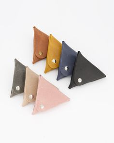 four different colored triangle shaped leather cases on a white surface with two holes in the middle