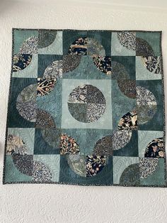 a blue and green quilt hanging on the wall