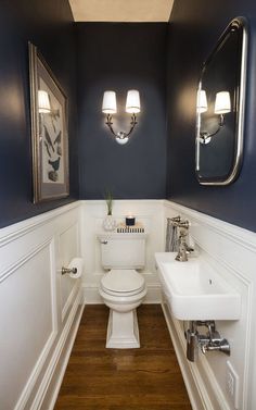 a white toilet sitting next to a sink in a bathroom under two framed pictures on the wall