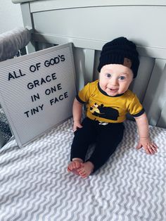 a baby sitting on top of a bed next to a sign that says all of god's grace in one tiny face