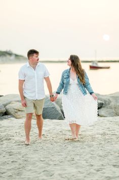 an engaged couple walking on the beach holding hands