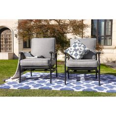 two gray chairs sitting on top of a blue and white rug in front of a building