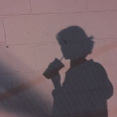 the shadow of a man holding a drink in his hand and standing next to a brick wall