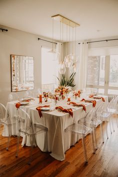 a dining room table is set with white linens and orange napkins