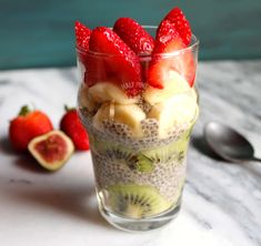 a glass filled with fruit on top of a table next to sliced kiwis