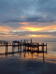 a boat is docked at the end of a pier as the sun sets over the water