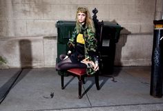 a woman sitting on top of a chair next to a trash can