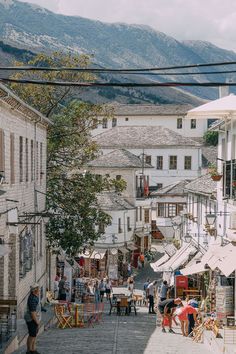 people are walking down the street in an old town with mountains in the background,