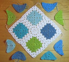 a crocheted square with blue and green leaves around it on a wooden floor