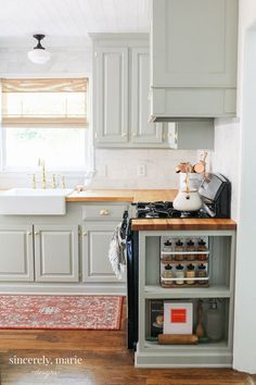 a kitchen with gray cabinets and white walls, wood flooring and an area rug