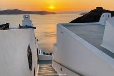 the sun is setting over an ocean with stairs leading up to it and some hills in the background