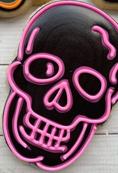 a decorated sugar cookie with neon pink icing and a black skull on the front