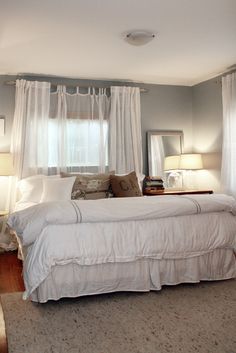 a bed sitting in a bedroom next to two lamps on either side of a window