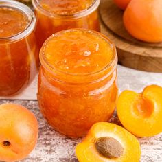 jars filled with jam sitting on top of a table next to sliced peaches and whole apricots