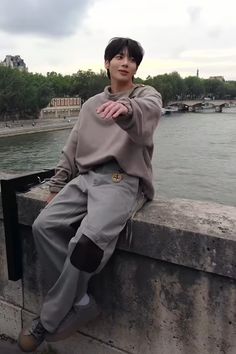 a young man sitting on the edge of a stone wall next to a body of water