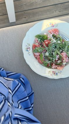 a white plate topped with salad sitting on top of a blue table cloth next to a knife and fork