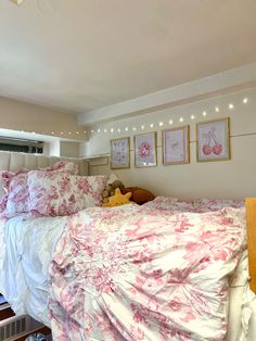 a bed with pink and white comforter in a bedroom next to a window filled with framed pictures