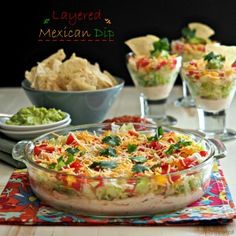 layered mexican dip with tortilla chips and guacamole in the background