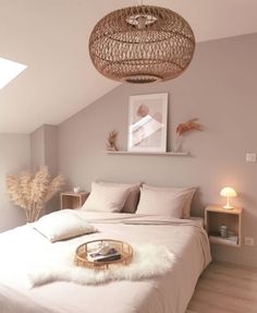 a white bed sitting under a light fixture in a bedroom next to a lamp shade