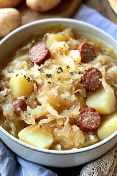 a white bowl filled with sausage and potatoes on top of a blue towel next to potatoes