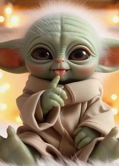 a baby yoda doll sitting on top of a fluffy white blanket with lights in the background