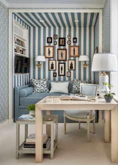 a living room with blue and white striped wallpaper, couches, lamps and pictures on the wall