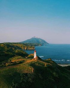 a lighthouse sitting on top of a lush green hillside next to the ocean with a mountain in the background