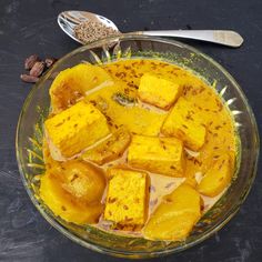 a glass bowl filled with cubed food next to spoons and nuts on a table