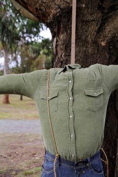 an old man with his arms stretched out in front of a tree wearing a green shirt and jeans