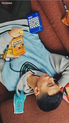 a young boy laying on top of a brown couch next to a pile of children's books