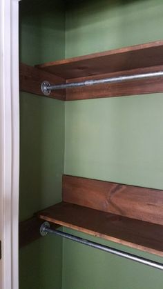 an empty closet with wooden shelves and metal bars on the bottom, along with green walls