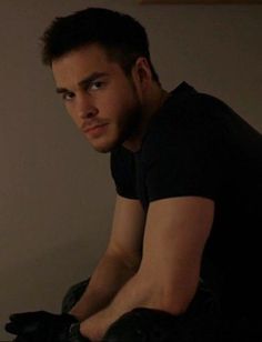 a man in black shirt sitting on top of a chair next to a wall and looking at the camera