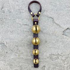 a leather key chain with three brass bells on it, sitting on a stone surface