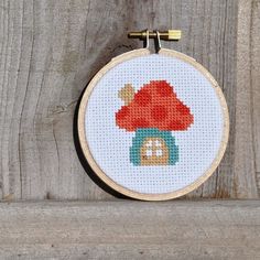 a cross - stitch mushroom is hanging on the side of a wooden fence with a bell