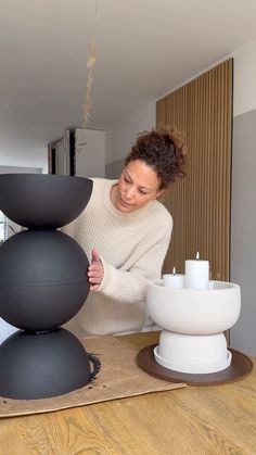 a woman standing next to a stack of balls on top of a wooden table