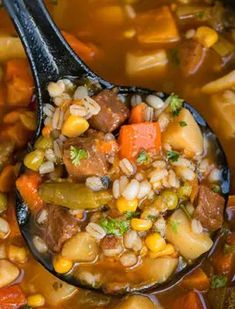 a spoon full of soup with beans, carrots and other food items in it