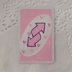 a pink card with an arrow drawn on it and hearts around the edges, sitting on a white tablecloth