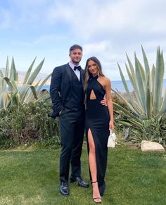 a man and woman in formal wear standing next to each other on the grass near some plants