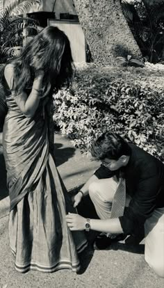 a man kneeling down next to a woman in a brown sari and blue shirt